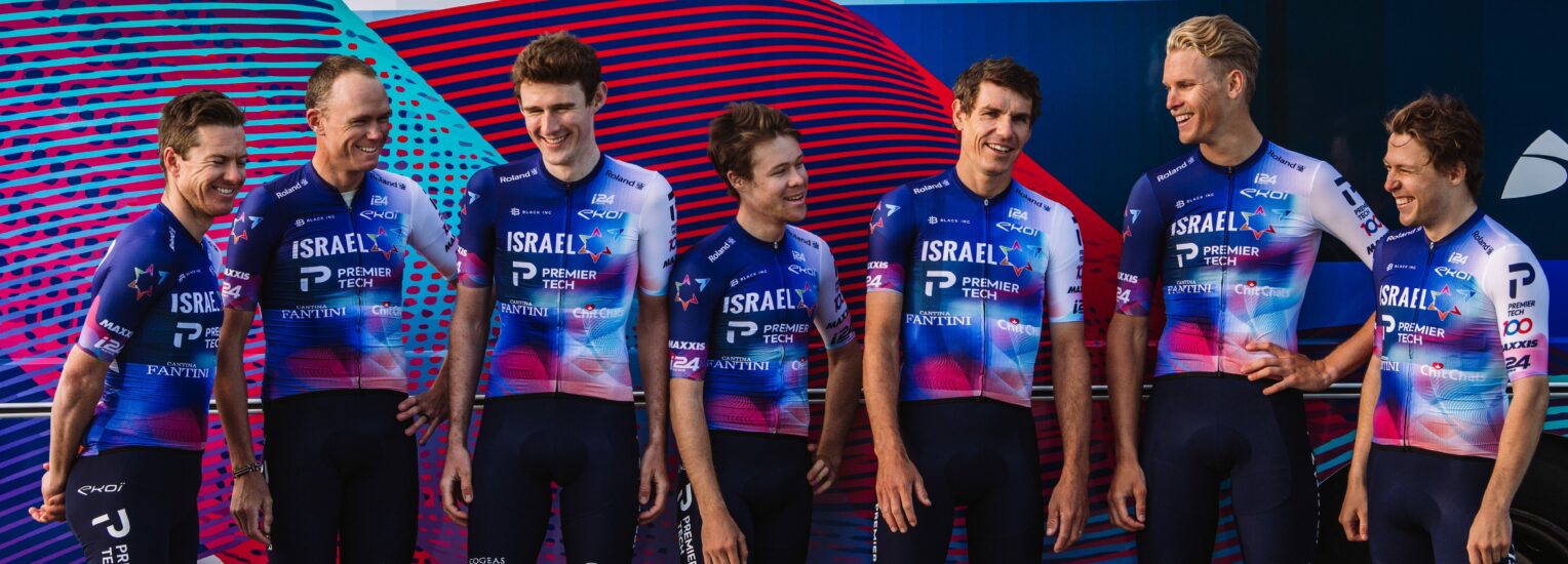 Israel Premier Tech team riders in 2023 kit standing in front of a team bus, 2022.
